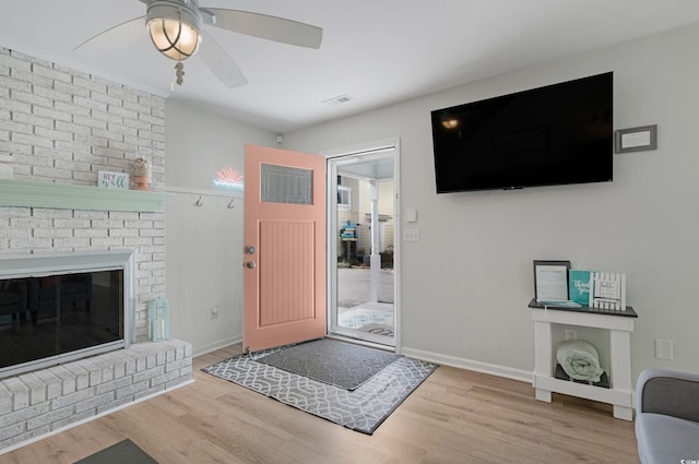 foyer featuring wood finished floors, a ceiling fan, visible vents, baseboards, and a brick fireplace