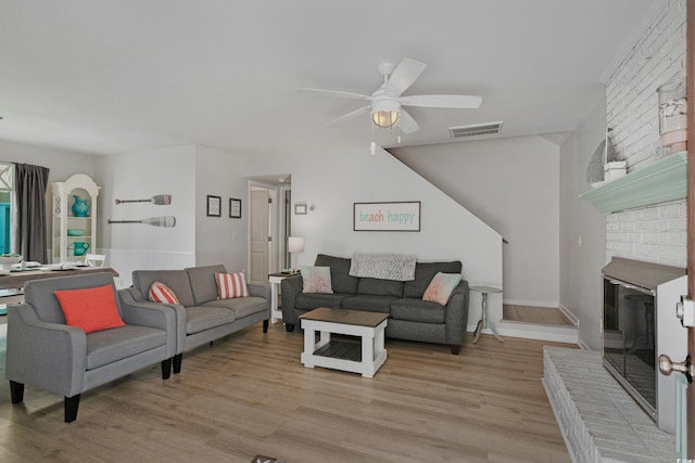 living area featuring light wood-style floors, visible vents, a fireplace, and a ceiling fan