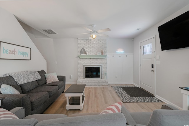 living room with a brick fireplace, ceiling fan, visible vents, and wood finished floors