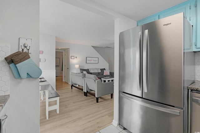 kitchen featuring light wood-style flooring, light stone countertops, freestanding refrigerator, and decorative backsplash