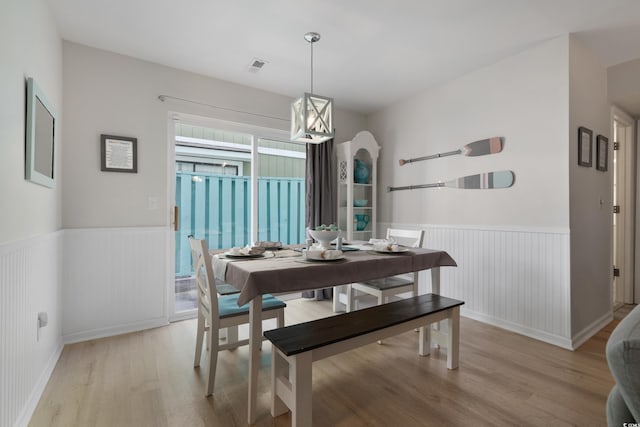 dining area featuring light wood finished floors, visible vents, arched walkways, and wainscoting