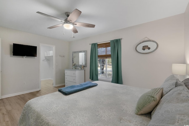 bedroom featuring a ceiling fan, a walk in closet, baseboards, and light wood finished floors