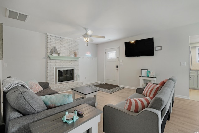 living room with ceiling fan, light wood-type flooring, a brick fireplace, and visible vents