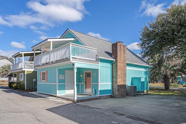 view of front of house with a shingled roof, a chimney, cooling unit, and a balcony