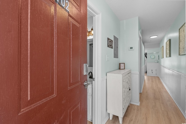 hallway with electric panel, a wainscoted wall, and light wood-style flooring