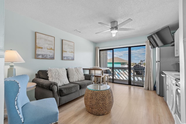 living area with visible vents, a textured ceiling, light wood-type flooring, and ceiling fan