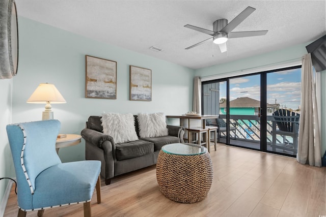 living room with a ceiling fan, wood finished floors, visible vents, and a textured ceiling