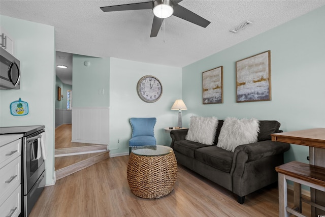 living room with visible vents, a wainscoted wall, a ceiling fan, a textured ceiling, and light wood finished floors