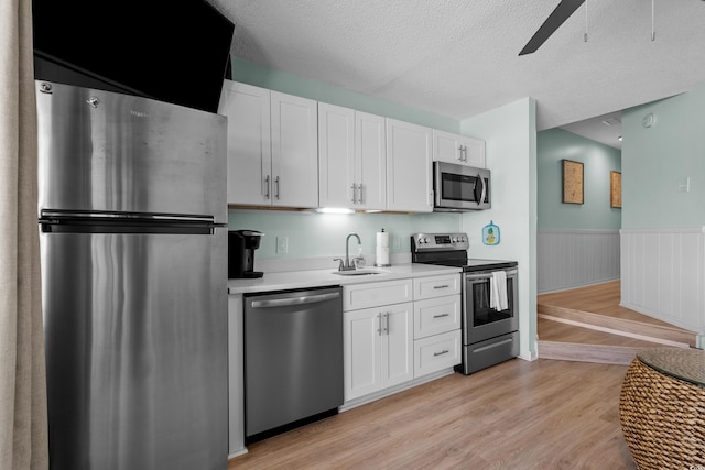 kitchen with a sink, light wood-style floors, appliances with stainless steel finishes, white cabinets, and wainscoting