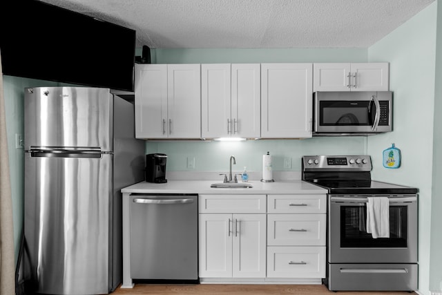 kitchen with a sink, light countertops, appliances with stainless steel finishes, a textured ceiling, and white cabinetry