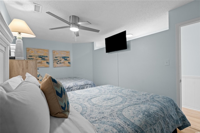 bedroom featuring visible vents, a textured ceiling, a ceiling fan, and wood finished floors