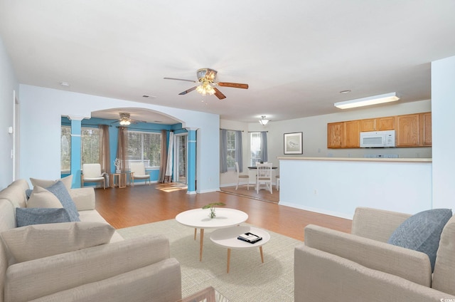 living area featuring baseboards, wood finished floors, decorative columns, and a ceiling fan