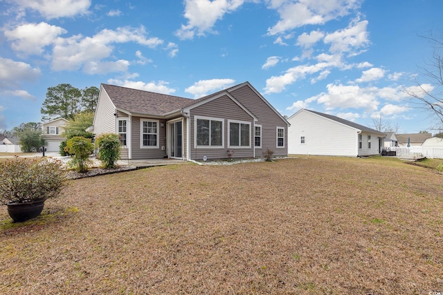 rear view of property with a shingled roof, a yard, and fence