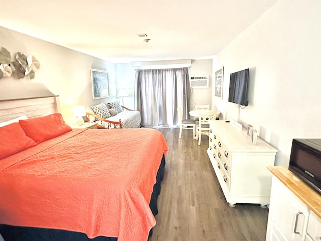 bedroom featuring wood finished floors, visible vents, and a wall mounted air conditioner