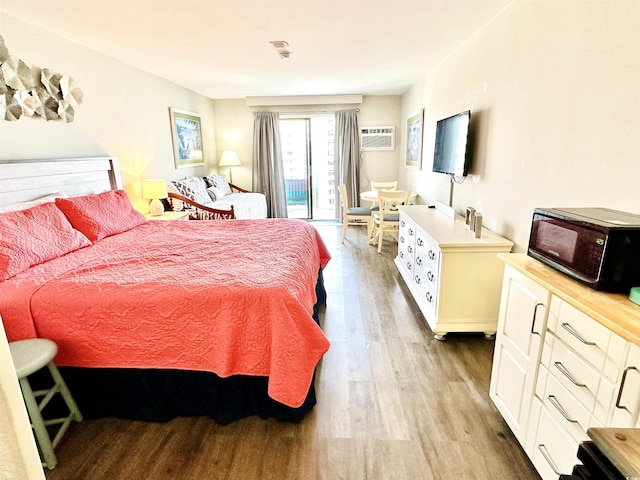 bedroom featuring access to outside, wood finished floors, and a wall mounted air conditioner