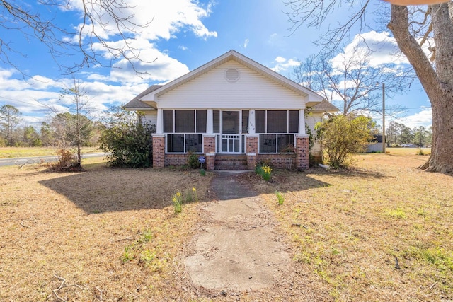 view of front of house featuring brick siding, a front lawn, and a sunroom