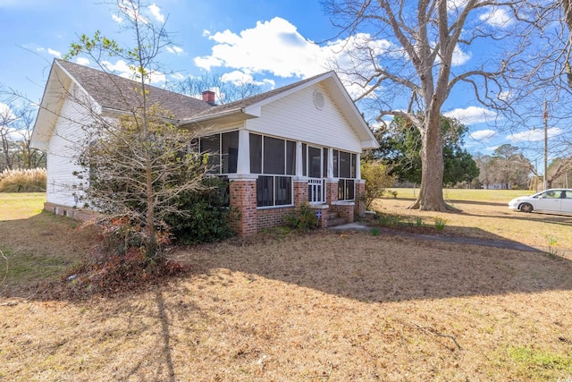 view of property exterior featuring brick siding, a chimney, a yard, and a sunroom