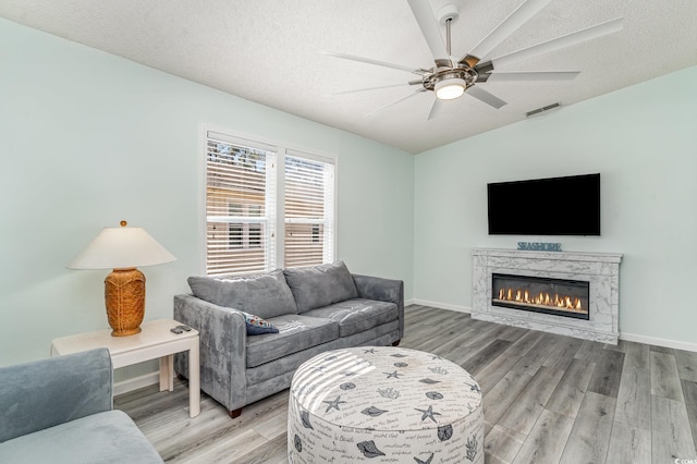 living room with light wood-type flooring, visible vents, a textured ceiling, and baseboards