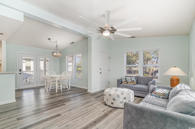 living room featuring vaulted ceiling, a textured ceiling, light wood-type flooring, baseboards, and ceiling fan with notable chandelier