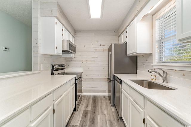 kitchen featuring wooden walls, white cabinetry, stainless steel appliances, and a sink