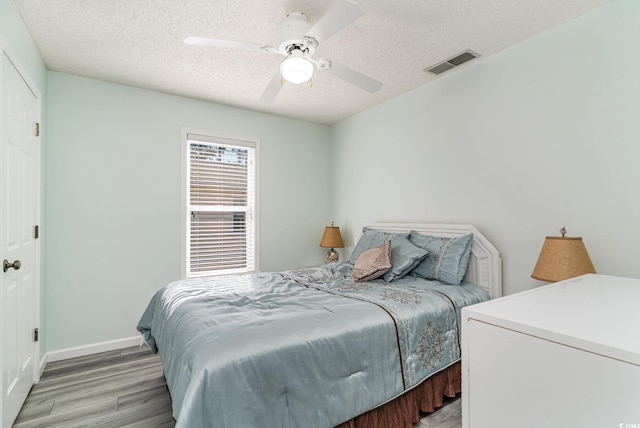 bedroom with a textured ceiling, ceiling fan, visible vents, baseboards, and light wood finished floors