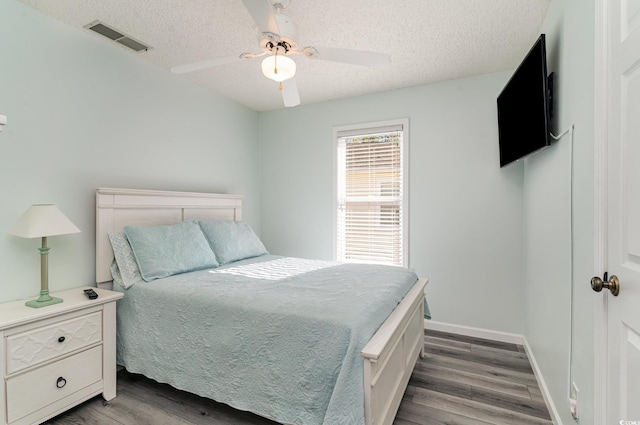 bedroom with visible vents, a textured ceiling, baseboards, and wood finished floors