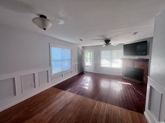 unfurnished living room featuring visible vents, ceiling fan, wood-type flooring, a fireplace, and a decorative wall