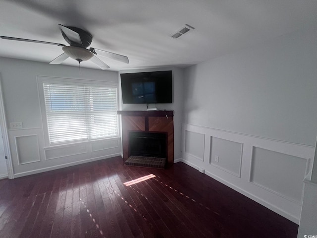 unfurnished living room with visible vents, a fireplace with raised hearth, a decorative wall, a ceiling fan, and hardwood / wood-style flooring