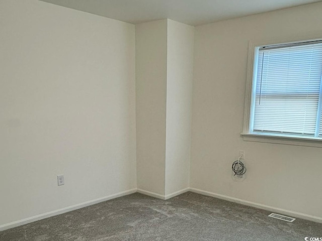 empty room featuring carpet, a healthy amount of sunlight, visible vents, and baseboards