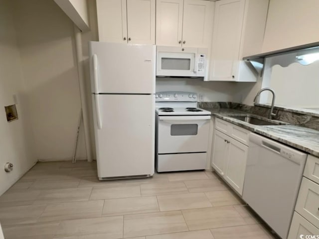 kitchen with white appliances, stone counters, a sink, and white cabinetry