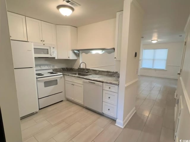 kitchen with white appliances, a sink, visible vents, baseboards, and white cabinets