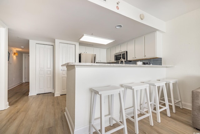 kitchen featuring appliances with stainless steel finishes, light wood-type flooring, a peninsula, and baseboards