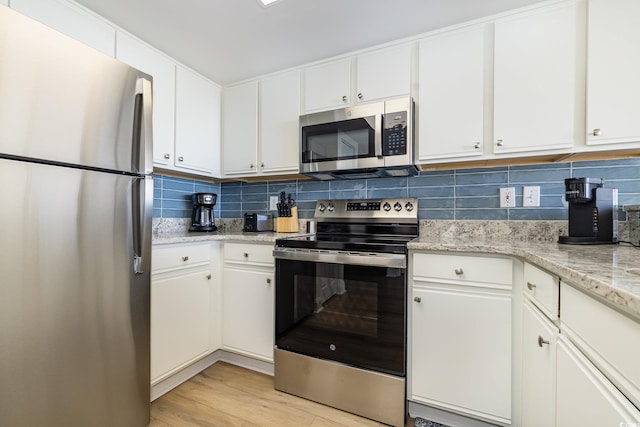 kitchen featuring appliances with stainless steel finishes, white cabinetry, light wood-type flooring, and backsplash