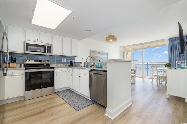 kitchen with stainless steel appliances, light wood-style floors, tasteful backsplash, white cabinetry, and a peninsula