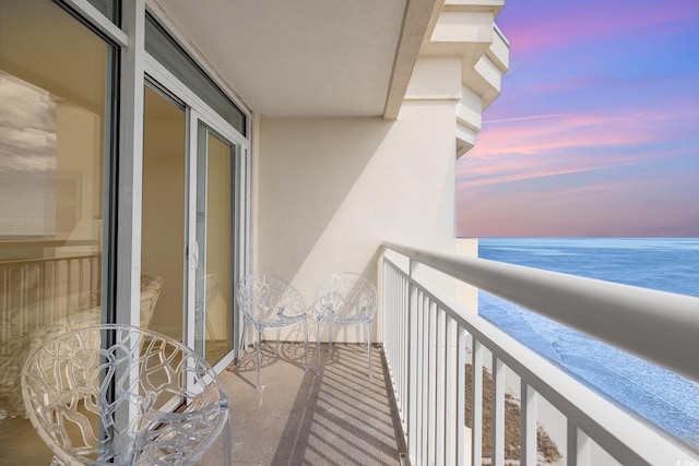 balcony at dusk featuring a water view