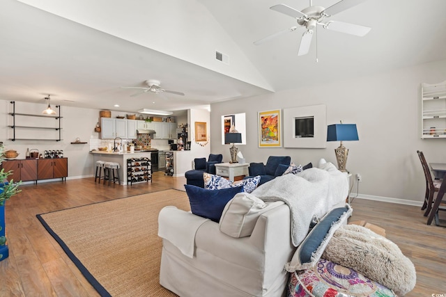 living room with wood finished floors, visible vents, baseboards, vaulted ceiling, and a ceiling fan