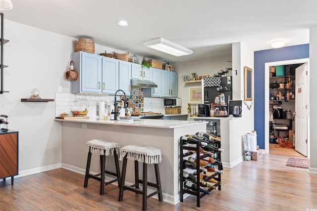 kitchen with white microwave, a peninsula, light countertops, blue cabinetry, and a kitchen bar