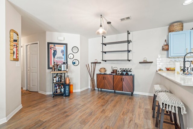 kitchen with blue cabinets, wood finished floors, visible vents, baseboards, and tasteful backsplash