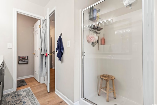 full bathroom with wood finished floors, a shower stall, vanity, and baseboards