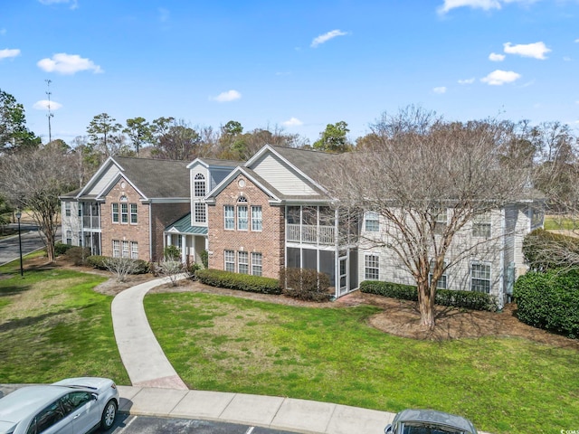 view of front of property with uncovered parking, a sunroom, brick siding, and a front lawn