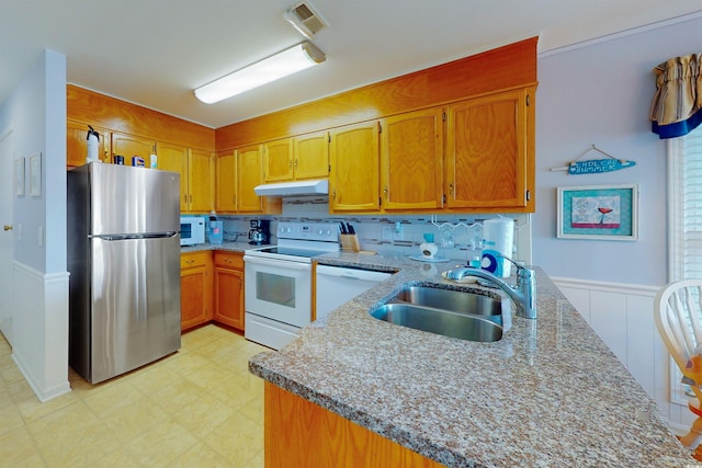 kitchen featuring under cabinet range hood, a peninsula, white appliances, a sink, and light floors