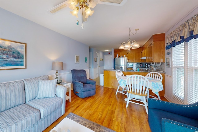 living room with light wood-style floors, wainscoting, and ceiling fan with notable chandelier