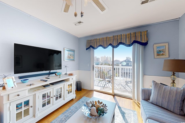 living area featuring light wood-type flooring, a wainscoted wall, ceiling fan, and visible vents