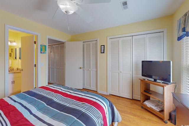 bedroom with ceiling fan, connected bathroom, wood finished floors, visible vents, and two closets