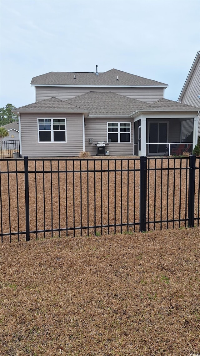 back of house with a fenced backyard, a sunroom, and roof with shingles