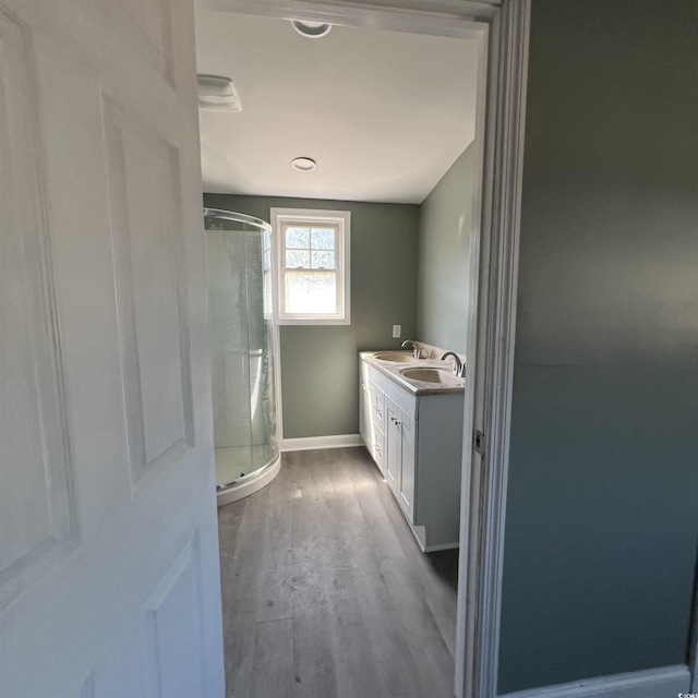 full bath featuring baseboards, vanity, wood finished floors, and a shower stall