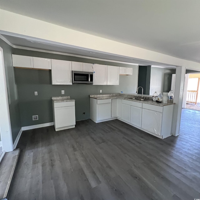 kitchen with baseboards, a sink, dark wood-type flooring, white cabinetry, and stainless steel microwave