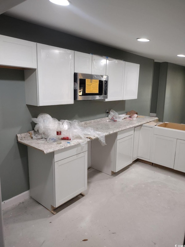 kitchen with stainless steel microwave, white cabinets, light countertops, and concrete floors