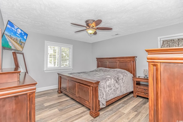 bedroom with light wood finished floors, visible vents, baseboards, ceiling fan, and a textured ceiling