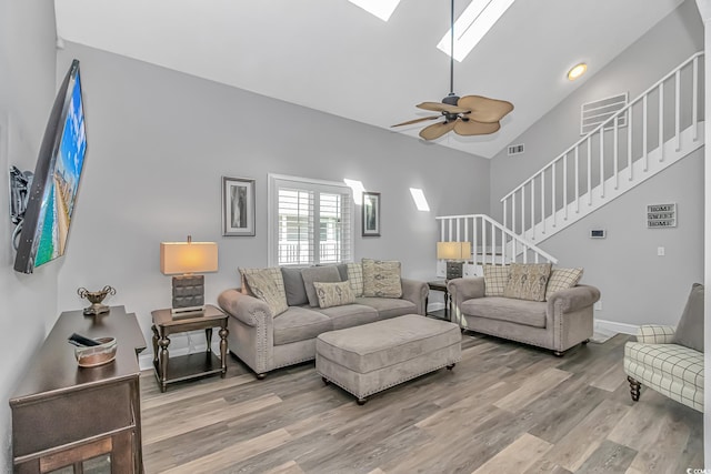 living area featuring a skylight, ceiling fan, wood finished floors, stairs, and high vaulted ceiling